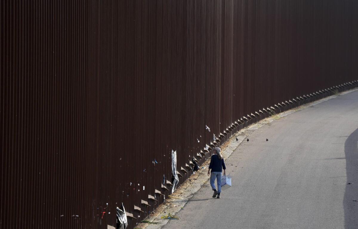 A volunteer walks along a border wall as she passes out baby wipes to migrants waiting to apply for asylum between two border walls Thursday, May 11, 2023, in San Diego. (AP Photo/Gregory Bull)