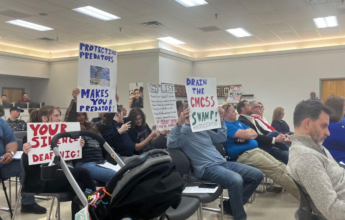 Attendees holding signs up toward the board at the CMCSS formal school board meeting on March 24, 2026. (Jazmin Logan)