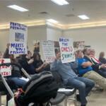 Attendees holding signs up toward the board at the CMCSS formal school board meeting on March 24, 2026. (Jazmin Logan)