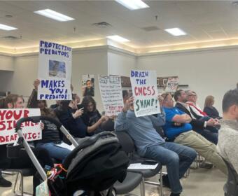 Attendees holding signs up toward the board at the CMCSS formal school board meeting on March 24, 2026. (Jazmin Logan)
