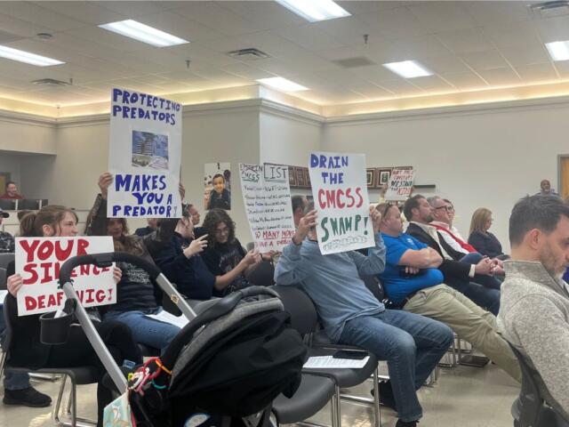 Attendees holding signs up toward the board at the CMCSS formal school board meeting on March 24, 2026. (Jazmin Logan)