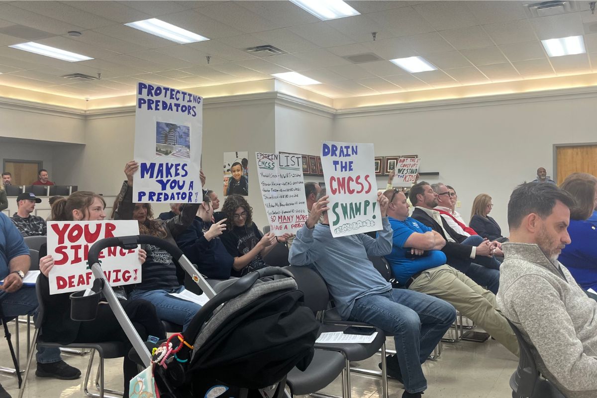 Attendees holding signs up toward the board at the CMCSS formal school board meeting on March 24, 2026. (Jazmin Logan)