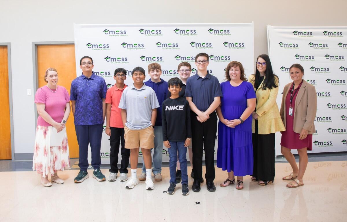 Group of students and adults posing together for a photo in front of a CMSS backdrop.