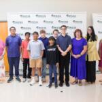 Group of students and adults posing together for a photo in front of a CMSS backdrop.