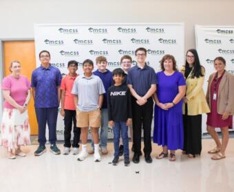 Group of students and adults posing together for a photo in front of a CMSS backdrop.