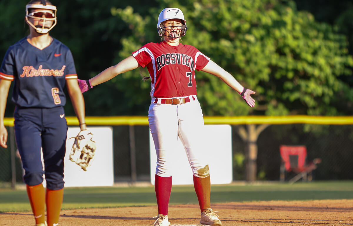 Softball player in a red Rossville uniform at first base with arms outstretched; teammate in navy stands nearby with a glove.