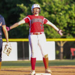 Softball player in a red Rossville uniform at first base with arms outstretched; teammate in navy stands nearby with a glove.