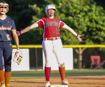 Softball player in a red Rossville uniform at first base with arms outstretched; teammate in navy stands nearby with a glove.