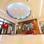 Interior lobby of a modern building with a circular illuminated ceiling light and glass double doors at left; reception area with a wooden wall and sign reading 'LARRY W. CARROLL FINANCIAL TRADING CENTER' in the background.