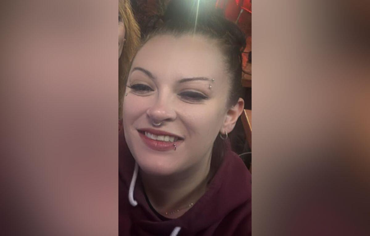 Smiling woman with a nose ring and eyebrow piercing wearing a maroon hoodie.