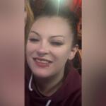 Smiling woman with a nose ring and eyebrow piercing wearing a maroon hoodie.