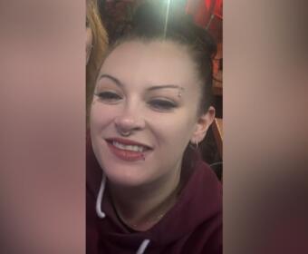 Smiling woman with a nose ring and eyebrow piercing wearing a maroon hoodie.