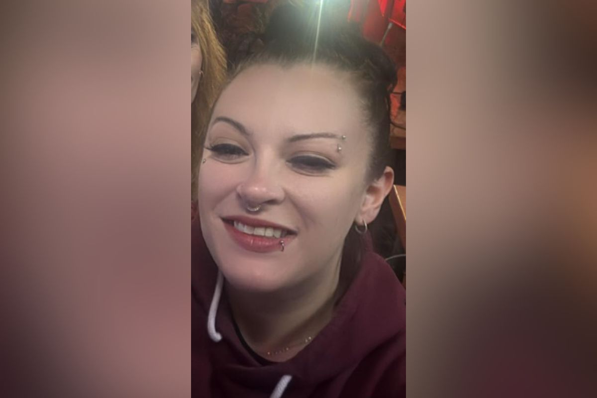 Smiling woman with a nose ring and eyebrow piercing wearing a maroon hoodie.