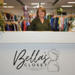 Smiling woman stands behind a white front desk at Bella's Closet, a women’s clothing store.