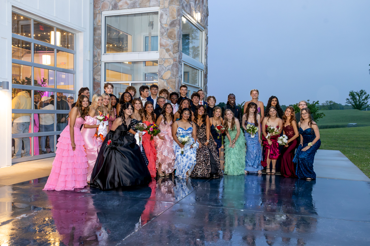 Group of teens in formal gowns and suits posing outside a modern venue after prom session.