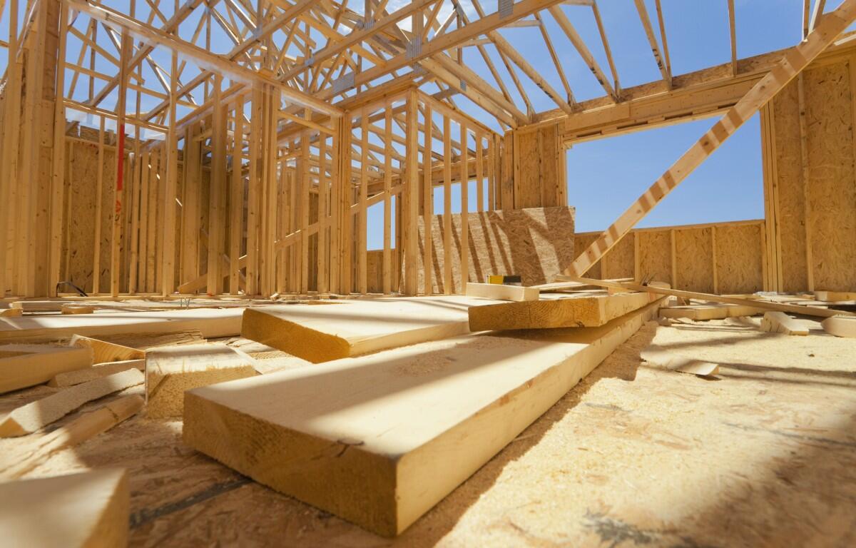 Interior of a timber-frame house under construction with exposed roof trusses and scattered wooden planks on the floor.