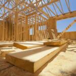 Interior of a timber-frame house under construction with exposed roof trusses and scattered wooden planks on the floor.