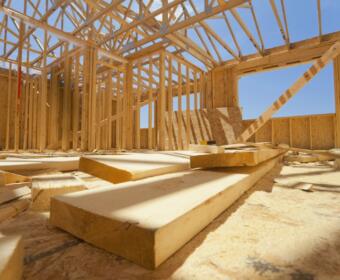 Interior of a timber-frame house under construction with exposed roof trusses and scattered wooden planks on the floor.
