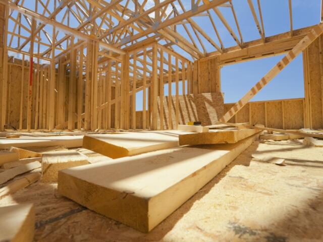 Interior of a timber-frame house under construction with exposed roof trusses and scattered wooden planks on the floor.