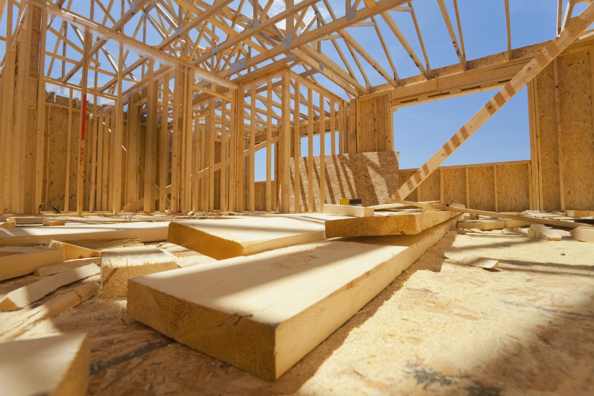 Interior of a timber-frame house under construction with exposed roof trusses and scattered wooden planks on the floor.