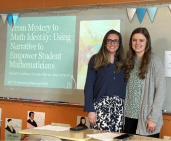 Two women pose in a classroom beside a projected slide about empowering student mathematicians in math identity research.