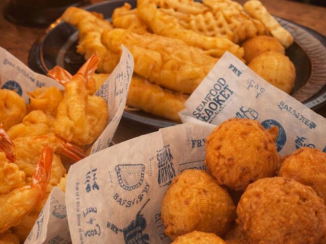 Assorted fried appetizers on a wooden table, including shrimp, hush puppies, and battered balls on parchment paper.