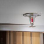 Close-up of a small recessed ceiling light fixture mounted to a white ceiling, showing metal housing and a red inner component.