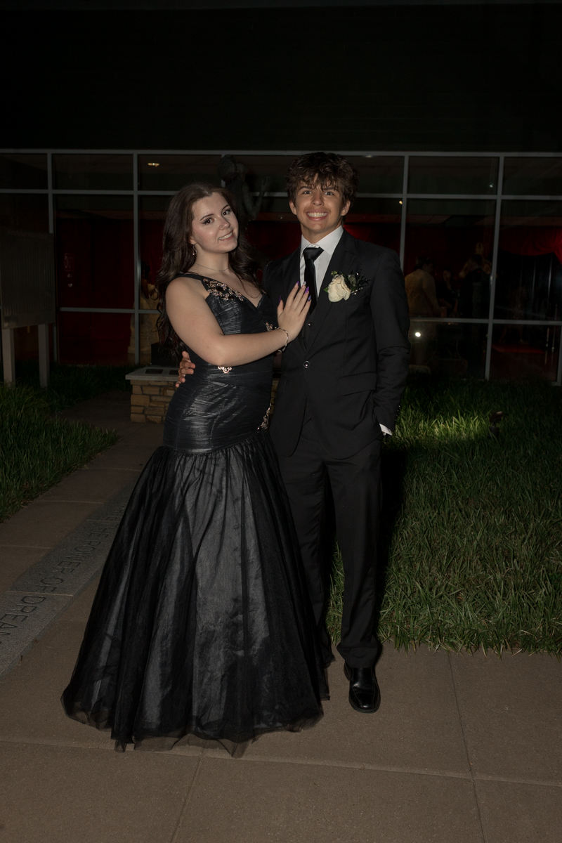 Couple dressed in formal wear pose together outdoors at night, smiling at the camera.