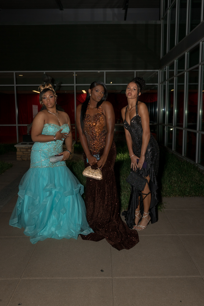 Three women in formal gowns posing outdoors at night, wearing turquoise, copper, and black dresses with matching clutches.