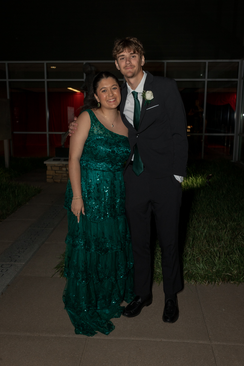 Couple posing outside at night; woman in emerald green sequined gown, man in black suit with green tie and white boutonniere.