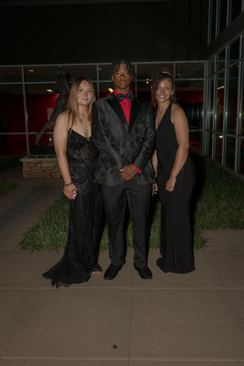 Three young adults in black-tie outfits posing outside a building at night.
