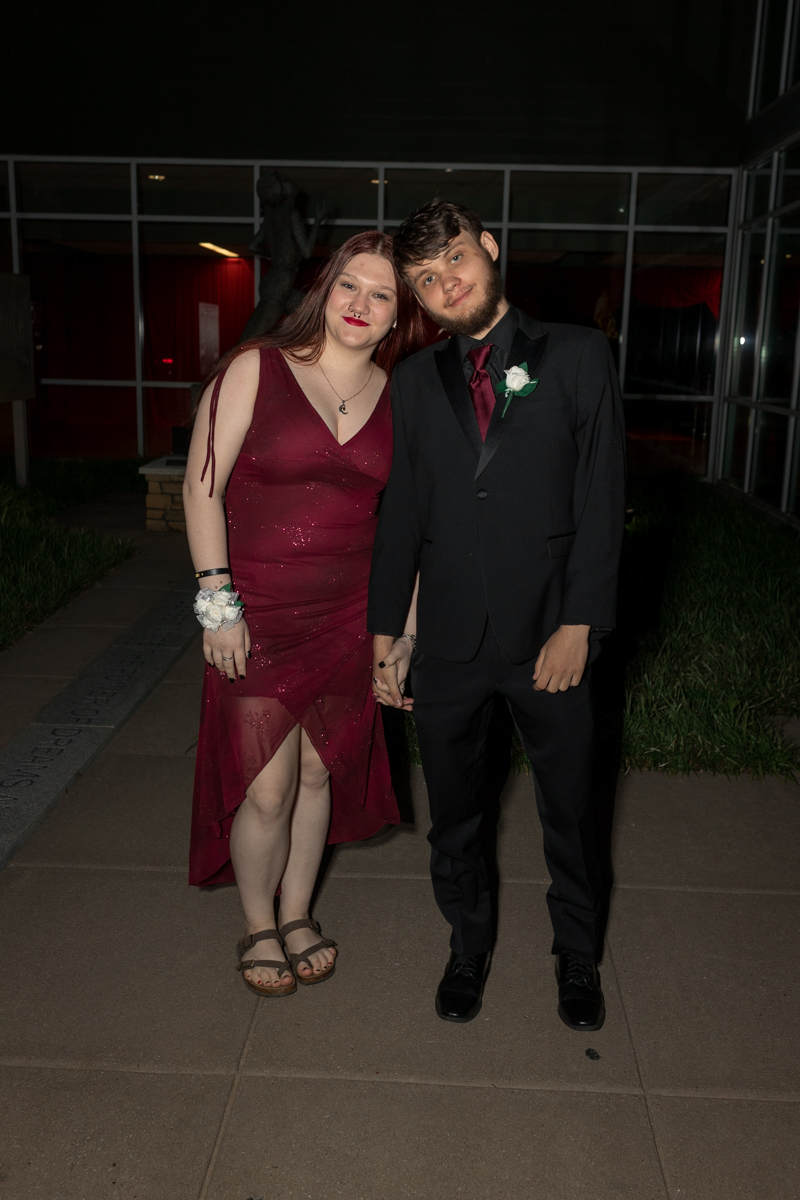 Couple in formal wear posing outdoors at night, holding hands and smiling at the camera.