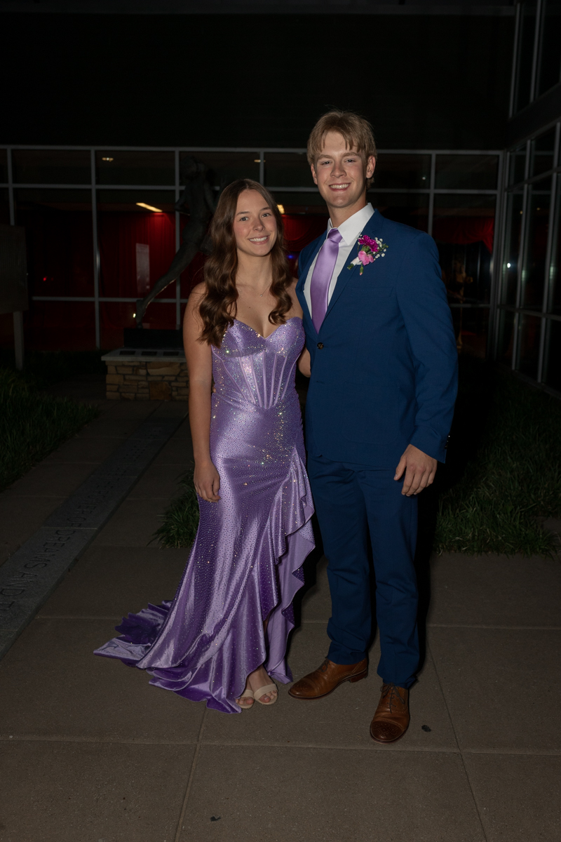 Young couple posing for a photo at a formal event; woman in a lavender sequined gown and man in a blue suit with pink tie and boutonniere.