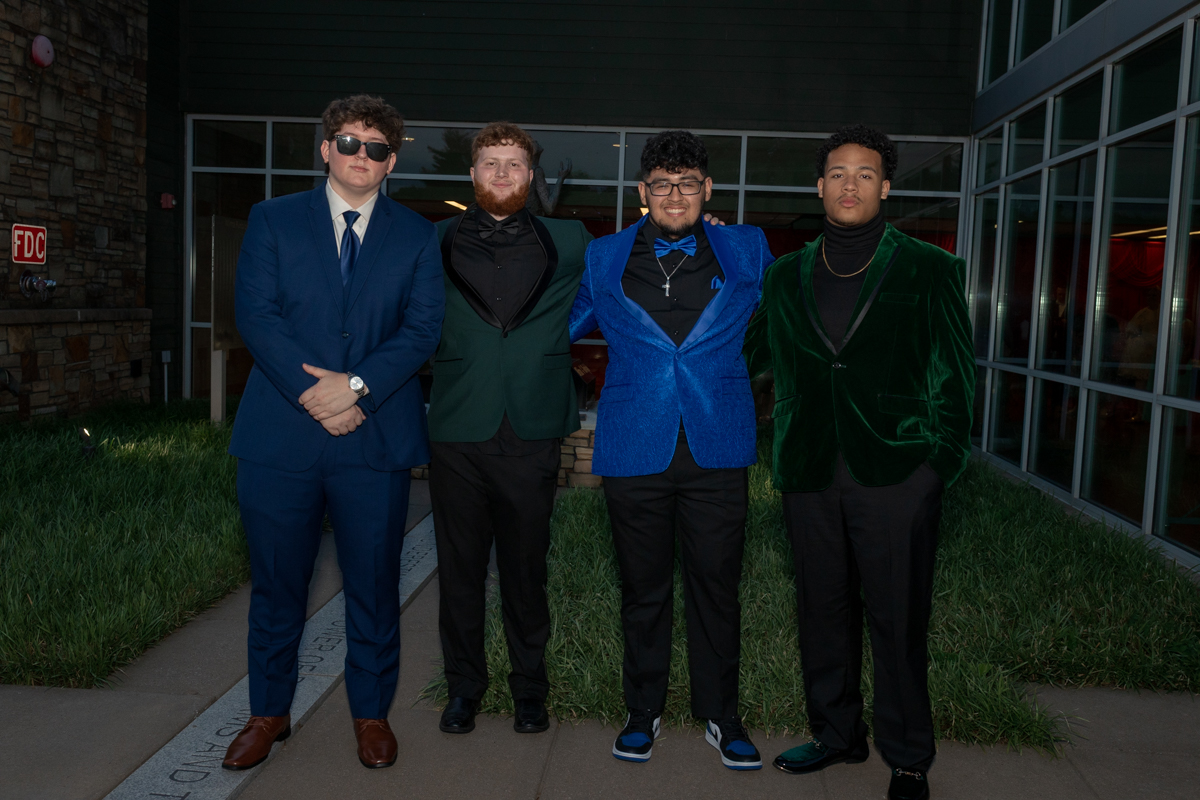 Four men in colorful velvet blazers pose together outside a building at night, looking at the camera.