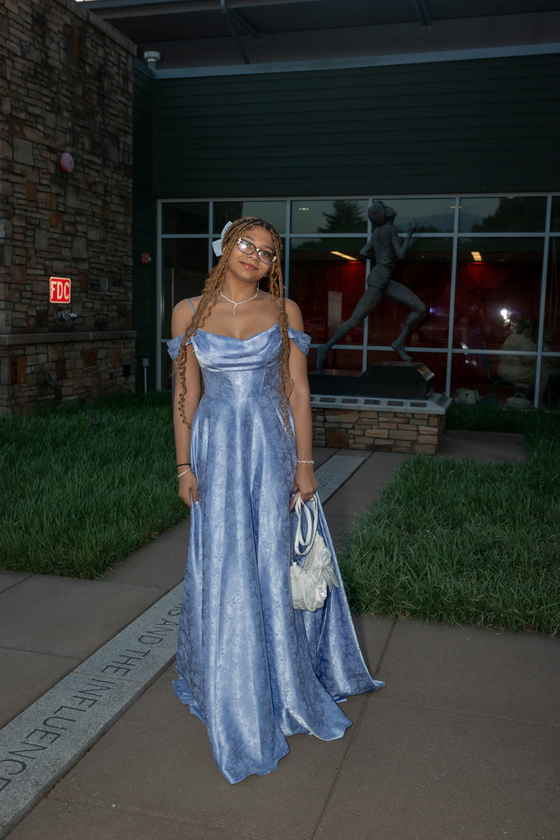 Young woman in a light blue off-shoulder ball gown standing outside a building with a statue in the background.