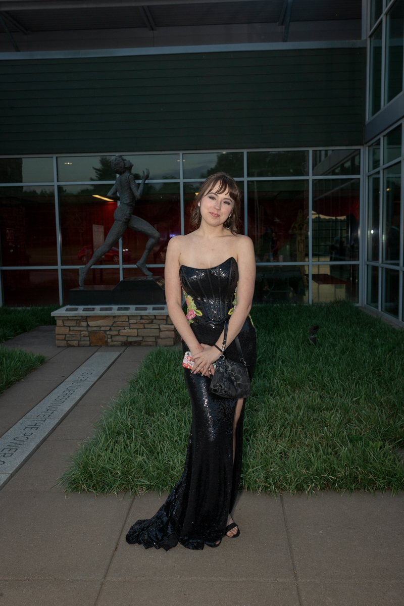 Portrait of a woman in a strapless black sequin gown posing outdoors near a sculpture and glass building.