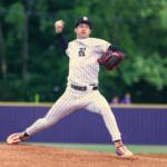 Baseball pitcher in a white pinstripe uniform winds up on the mound, throwing with his right arm, glove ready on his left hand.