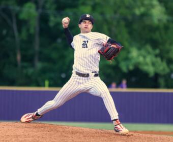 Baseball pitcher in a white pinstripe uniform winds up on the mound, throwing with his right arm, glove ready on his left hand.