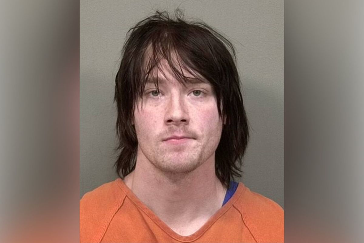 Mugshot of a man with shoulder-length dark hair in an orange prison jumpsuit against a gray background.