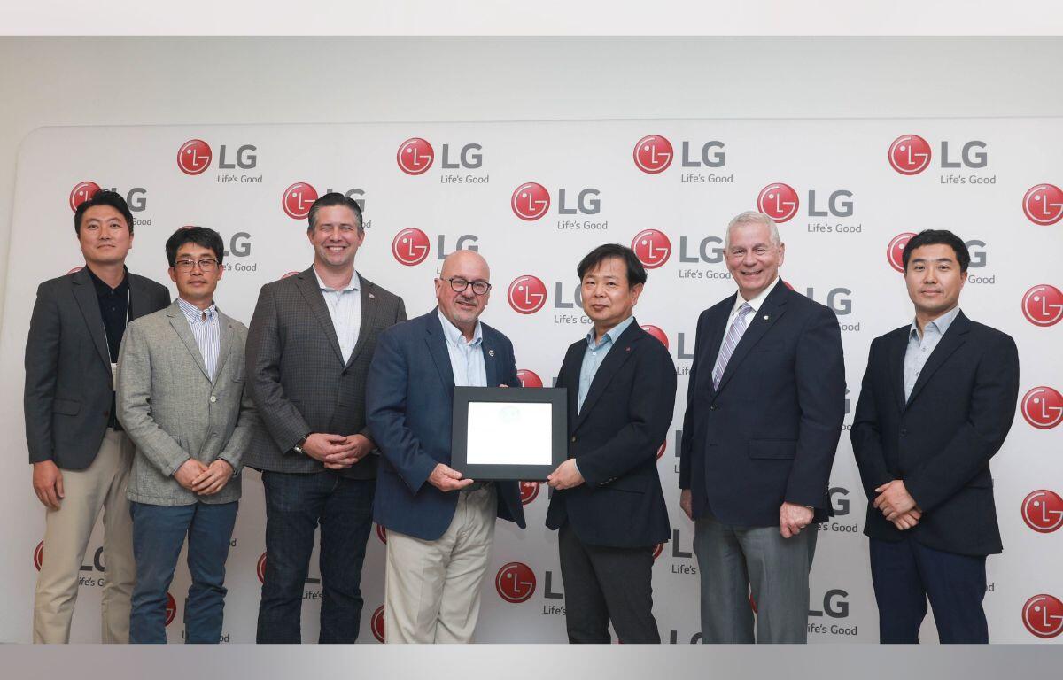 Seven men in business attire pose for a photo in front of an LG backdrop; two in the center hold a framed certificate as an award is presented.