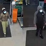 Two masked men enter a store through the entrance; left man wears camo hoodie and beige pants, white cap.