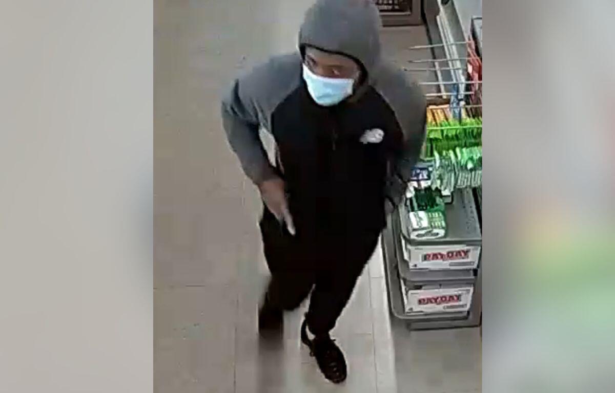 Person in a gray hoodie and face mask walking through a store aisle near shelves with products present