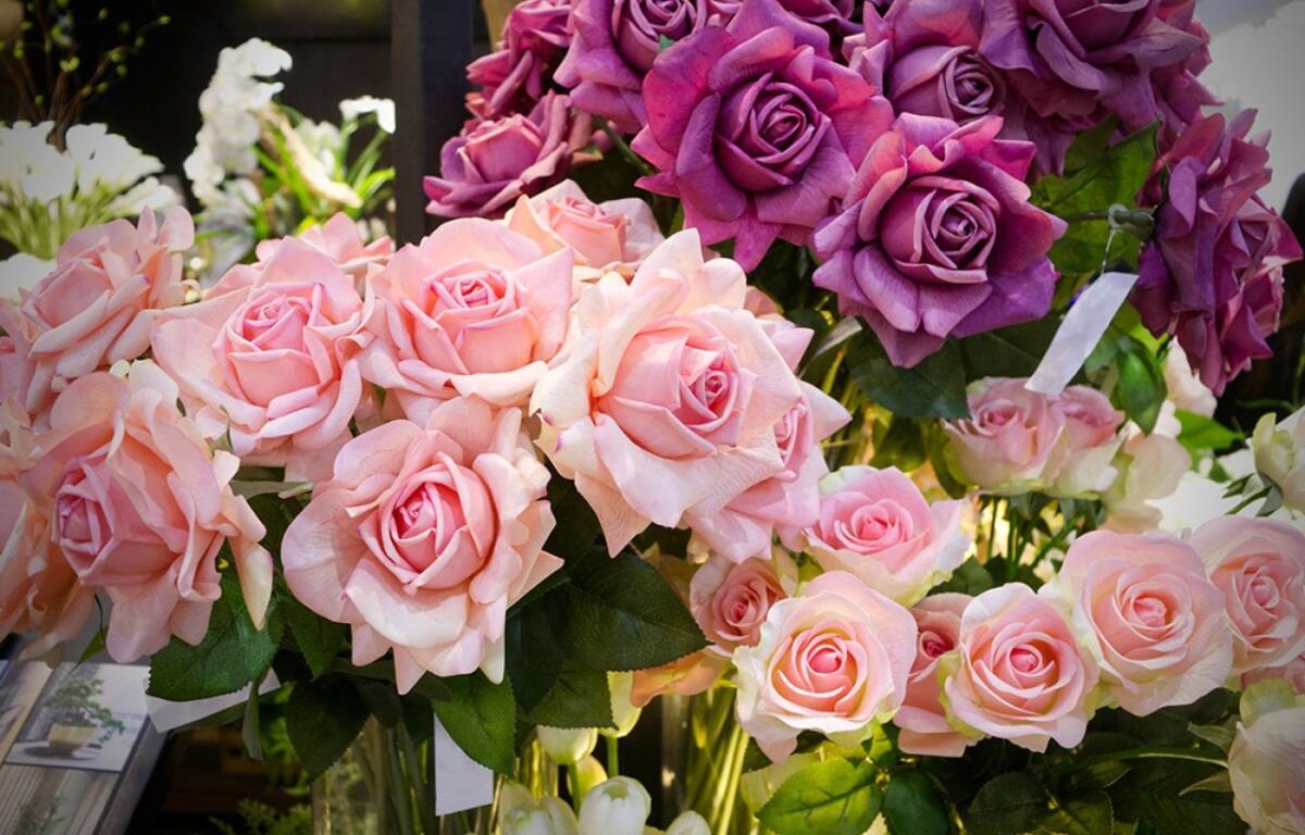 Vibrant display of pink and purple rose bouquets in a florist shop window.
