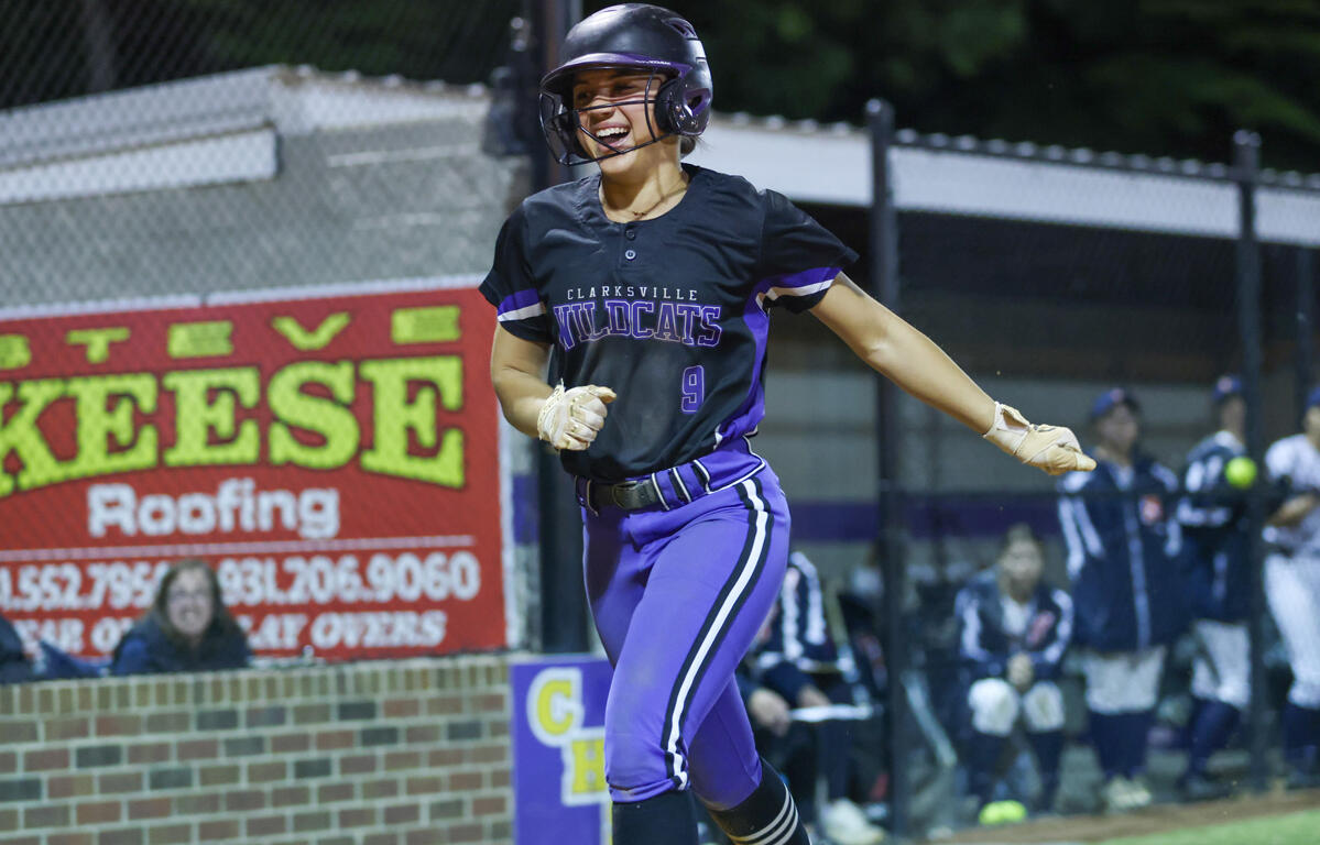 Female softball player in a black and purple Wildcats uniform, helmet, running on the bases during a game.