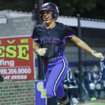 Female softball player in a black and purple Wildcats uniform, helmet, running on the bases during a game.