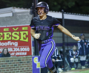 Female softball player in a black and purple Wildcats uniform, helmet, running on the bases during a game.