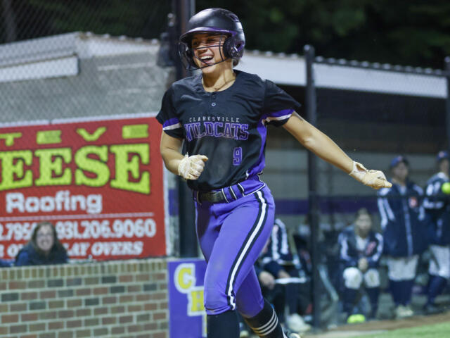 Female softball player in a black and purple Wildcats uniform, helmet, running on the bases during a game.