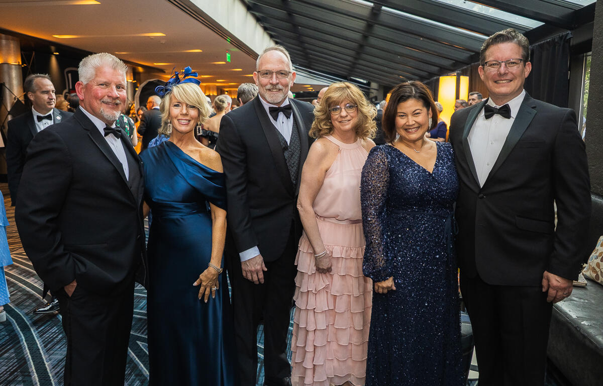 Six adults in formal evening wear posing for a group photo at a gala event.