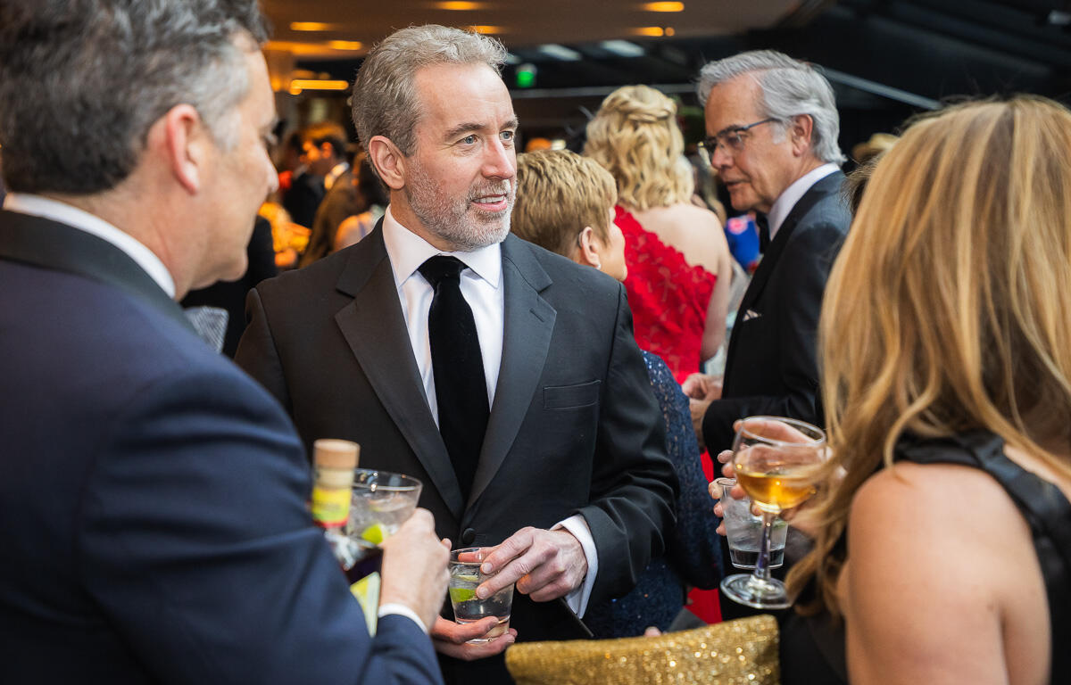 Group of formally dressed guests at a cocktail party, conversing and holding drinks in a crowded venue.
