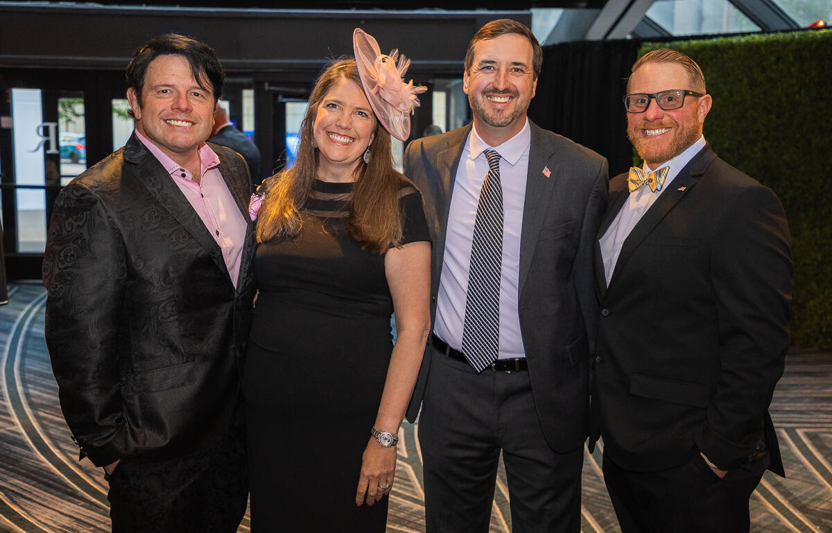 Four adults in formal attire posing together at an event, smiling for the camera.